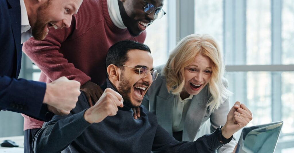 A diverse team in an office celebrates a successful achievement while looking at a laptop.